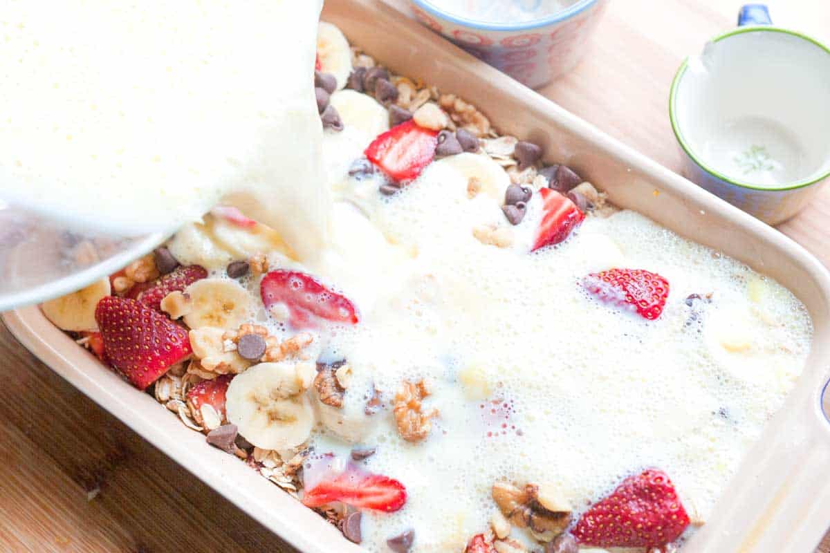 How to Make Strawberry Baked Oatmeal: Pouring the milk mixture into a baking dish with oats, sugar, and fruit.
