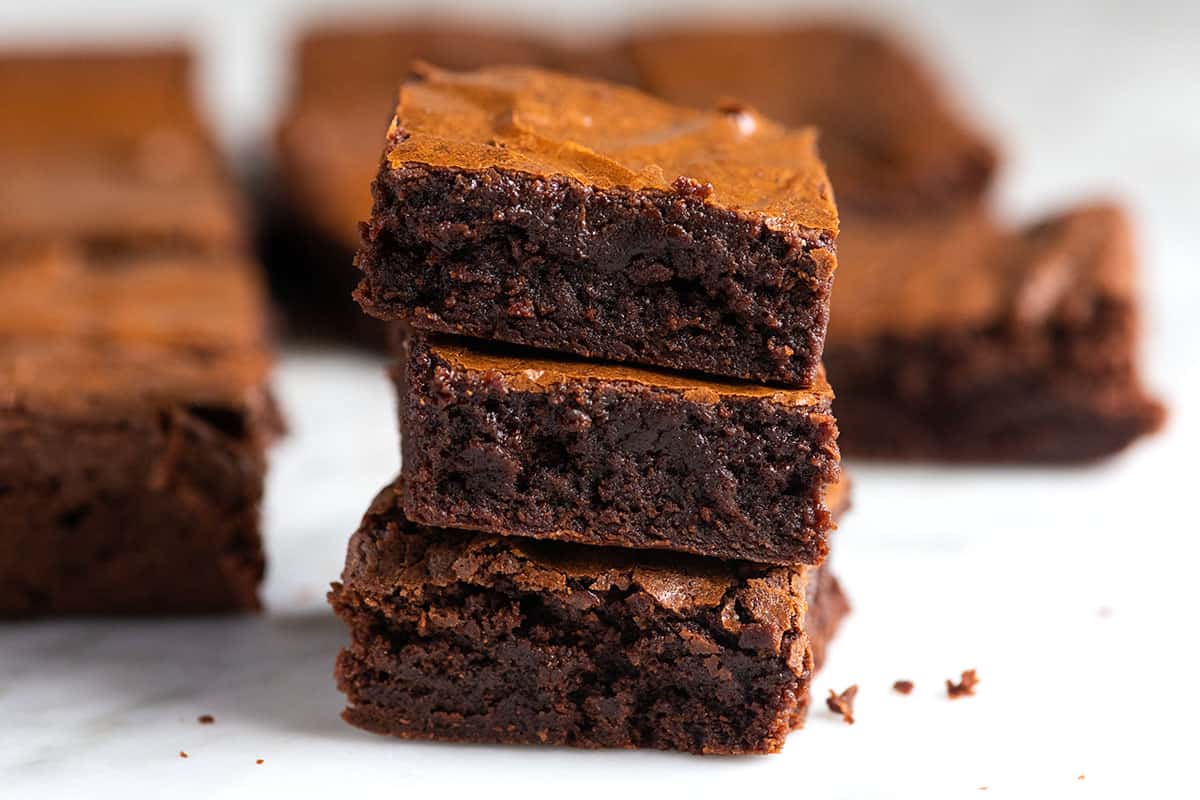 Stack of baked brownies made in one-bowl showing a crinkly top and chewy edges.
