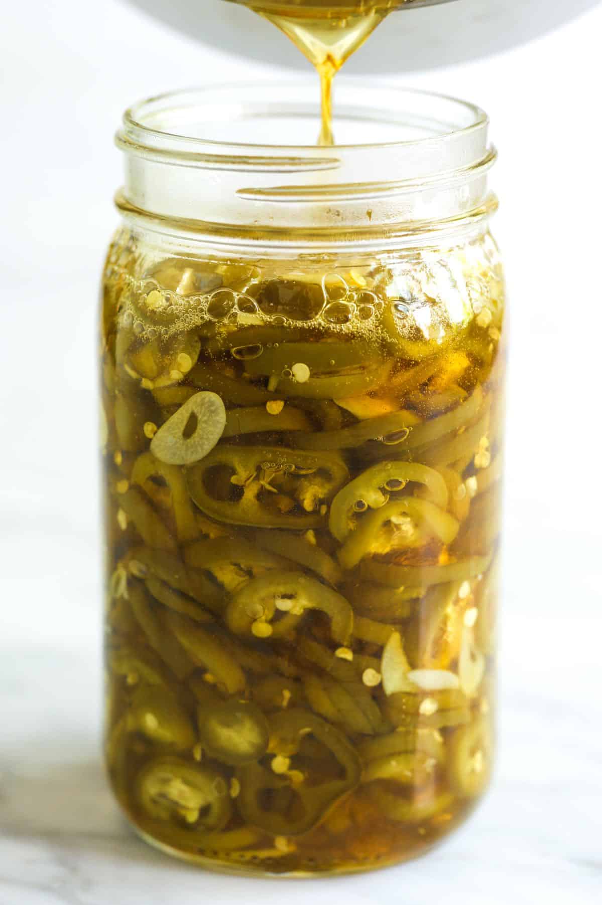 Making candied jalapeños - Pouring a sugar syrup into a jar with jalapeños and garlic.