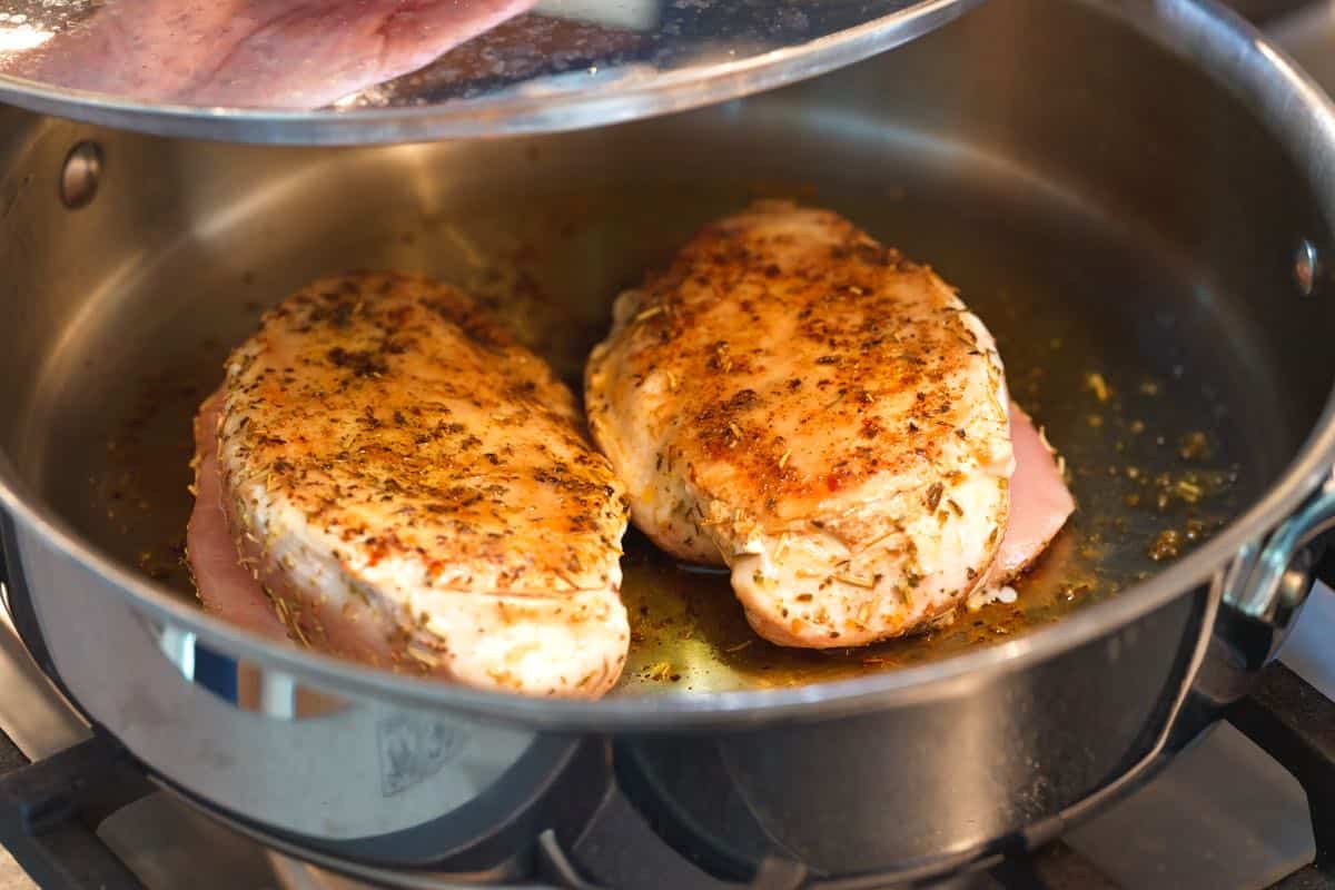 How to Make Chicken Alfredo: Cooking seasoned chicken breasts in a skillet.